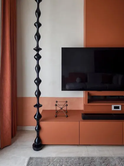The TV wall unit features a striking glossy black wooden turning that runs from floor to ceiling, contrasting with the textured matte finish of the wall.