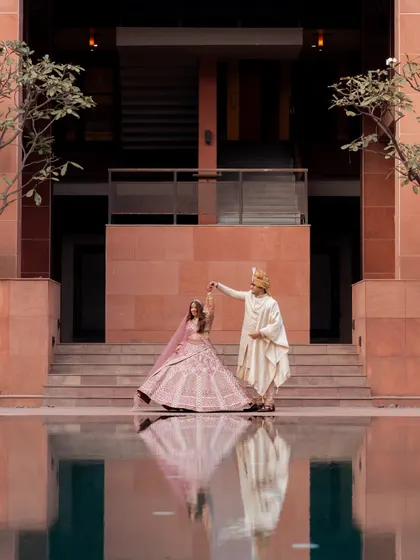 A dreamy destination wedding portrait with the couple's reflection in the still water of a pool. The modern architecture and their traditional attire create a stunning visual contrast.