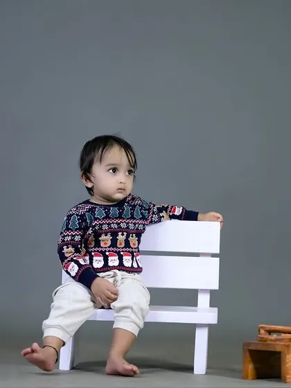 A cool and casual pose from a little boy on a white bench. The simple grey background creates a classic, timeless look.