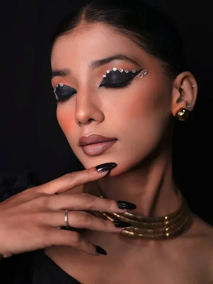 A dramatic pose with eyes closed, showcasing the intricate, sparkling eyeliner and the smooth, flawless makeup application.