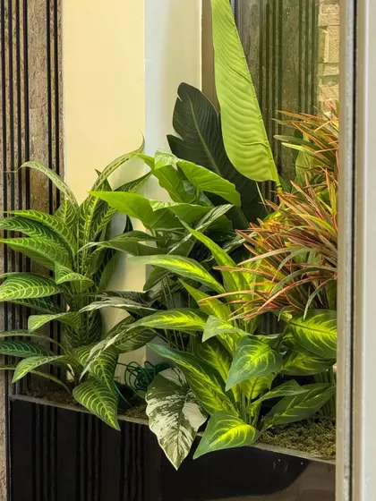A close-up of a lush, multi-layered artificial planter. The variety of leaf shapes and colors creates a dense, tropical feel that enlivens any corner.