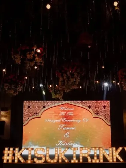 The stage is set for a grand Sangeet, with a custom LED screen and a large marquee sign of the couple's wedding hashtag.