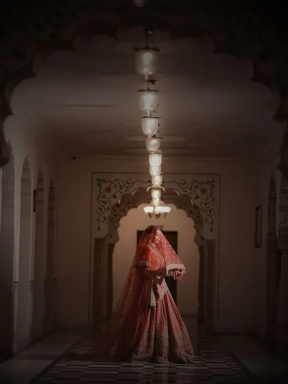 A low-light, moody portrait of the bride under her veil, creating a sense of anticipation and mystery in a grand palace corridor.