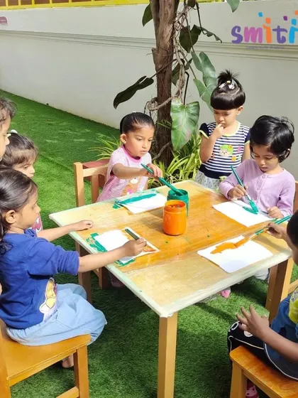 Children sit outdoors, painting their khadi flags. The natural setting enhances this creative and patriotic activity.