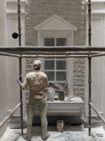 A craftsman at work inside the open-to-sky shaft of the KAIRA residence. This image captures the skilled labor involved in executing the detailed rubble masonry and classical mouldings.