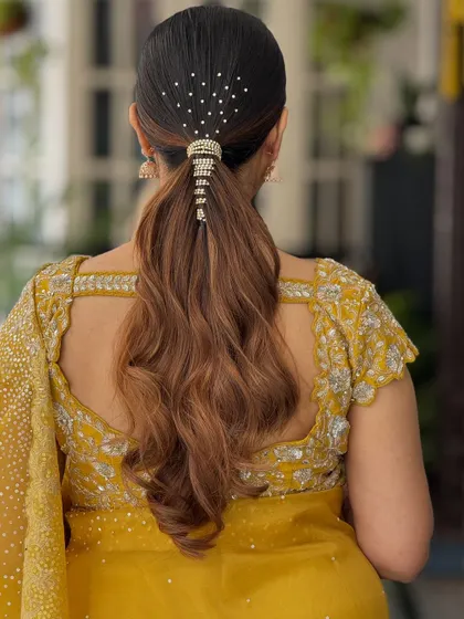 A sleek and chic low ponytail with a modern, embellished wrap. The scattered crystals on top add a touch of sparkle to this sophisticated look.