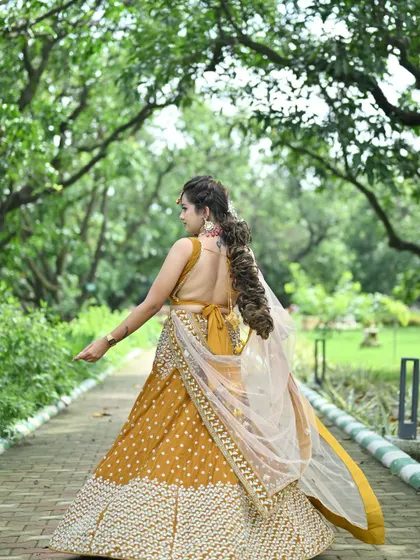 A back view of the mustard yellow lehenga, showcasing the low-back blouse design and the flow of the sheer dupatta.