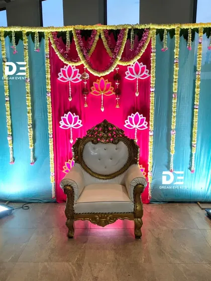 We created this vibrant baby shower stage using bright pink and blue drapes, accented with lotus cutouts and hanging floral strings for a festive and joyful look.