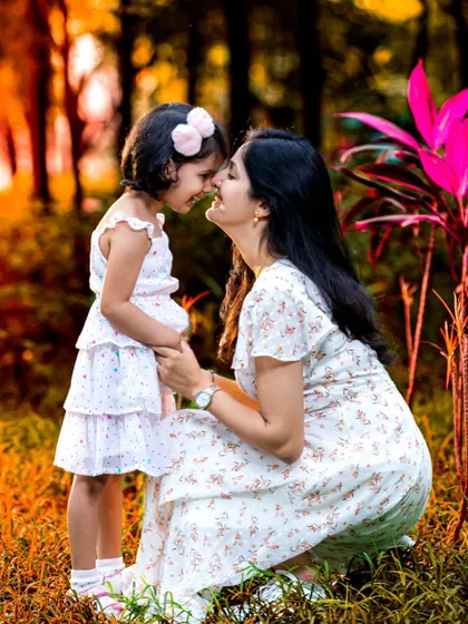 A mother and daughter share a sweet, gentle moment, touching noses in a beautiful outdoor setting. The warm sunset light adds a magical glow to this heartwarming portrait.
