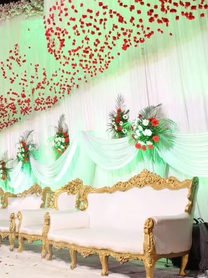 An elegant stage setup with white and gold sofas, against a backdrop of white drapes and red floral arrangements.
