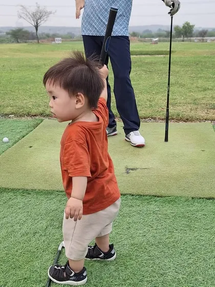 It is never too early to start. This little one is already getting a feel for the game, holding a golf club on the green with his father nearby.