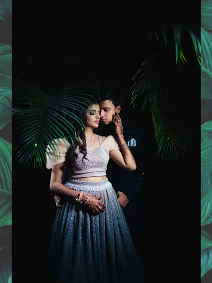 A moody and romantic pre-wedding portrait taken at night, with dramatic lighting highlighting the couple against dark foliage.