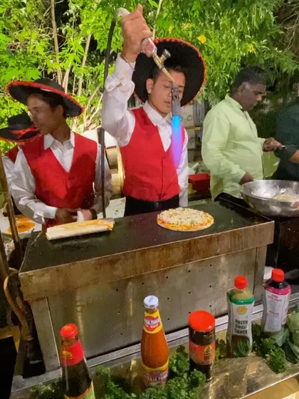 Freshly made pizza being topped with sauce at a live counter. This interactive station is perfect for sangeets and cocktail parties, offering a casual and delicious option.