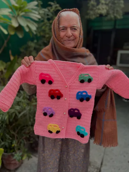 For the little car enthusiast. This pink cardigan is decorated with colorful, puffy crochet cars. It's a playful design that adds a pop of fun to a classic button-up sweater.
