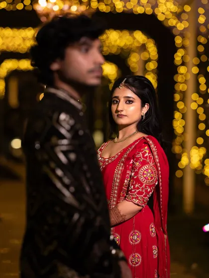 A creative composition with a shallow depth of field, focusing on the bride's expressive look as her partner stands in the foreground. The bokeh lights add a dreamy feel to this Sangeet night portrait.