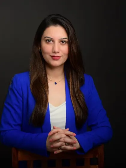 A seated professional headshot for a doctor. The calm expression and clasped hands convey a sense of empathy and professionalism.