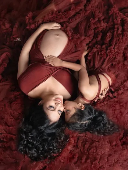 A tender moment between a mother and her daughter, eagerly awaiting the new arrival. This top-down perspective with a rich, textured gown creates a beautiful and intimate family maternity photo.