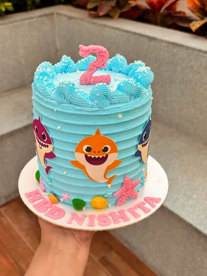 A bright blue Baby Shark cake with textured buttercream waves. The colorful shark characters and starfish make it a playful choice for a toddler's birthday.