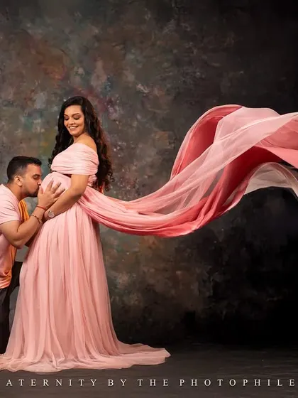 A classic studio portrait with a flowing pink gown, where the father-to-be tenderly kisses the baby bump. The fabric toss adds a beautiful, dynamic element.