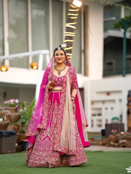 A beautiful outdoor portrait of the bride, her vibrant pink lehenga standing out against the natural background.