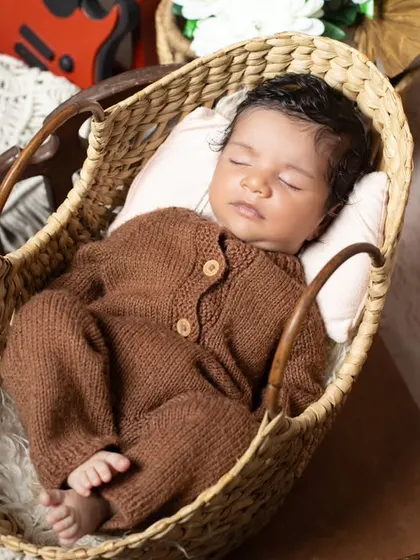 A cozy newborn in a brown knit outfit, sleeping soundly in a wicker basket.