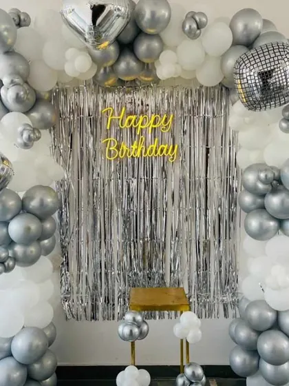 A disco-themed birthday backdrop with a silver and white balloon arch, disco ball foil balloons, and a silver foil curtain.