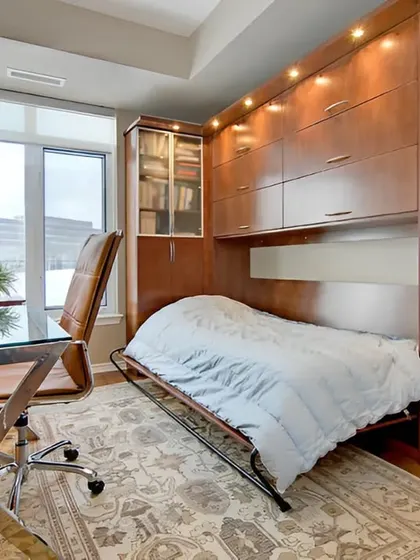 A practical guest room or home office featuring a Murphy bed. The bed folds up into a wooden cabinet unit, freeing up the floor space for a desk and chair during the day.