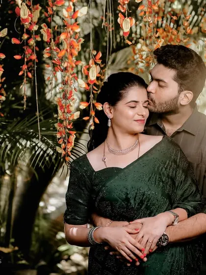 A romantic forehead kiss framed by lush greenery and hanging flowers, creating a dreamy, intimate portrait.