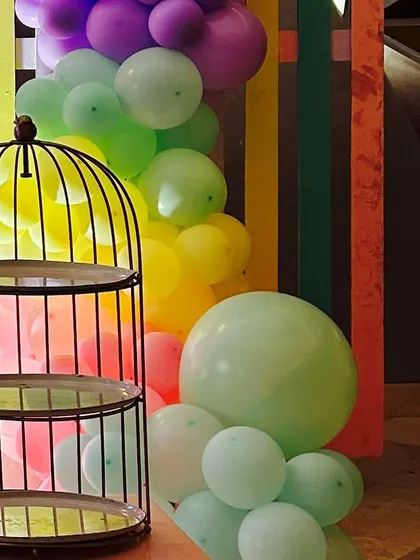 A detail shot of a rainbow themed party, featuring a colorful balloon cascade next to a decorative birdcage stand.