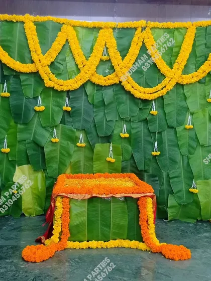 A classic and vibrant backdrop for a traditional Indian ceremony, such as a puja or Simmanta. This decoration is made entirely of fresh banana leaves and decorated with beautiful marigold flower garlands, creating an authentic and auspicious setting.