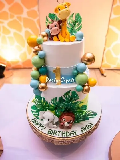 A close-up of the three-tiered safari cake for Ayra's first birthday. The adorable fondant animals and tropical leaves perfectly capture the 'Wild One' spirit.
