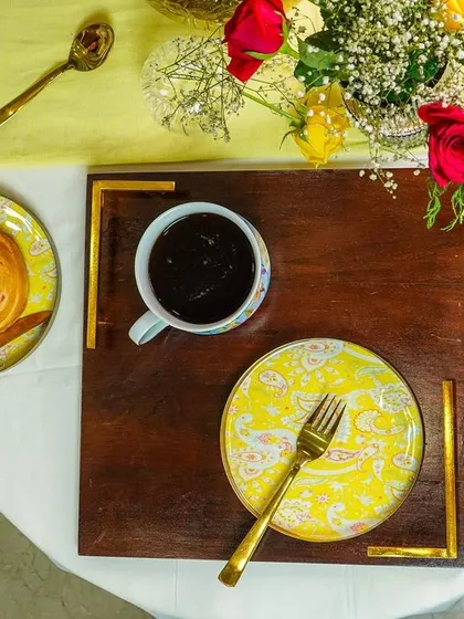 A top-down view of a breakfast-in-bed scene, with a pastry and coffee on a wooden tray. The human element of the hand reaching for the pastry adds a touch of life.