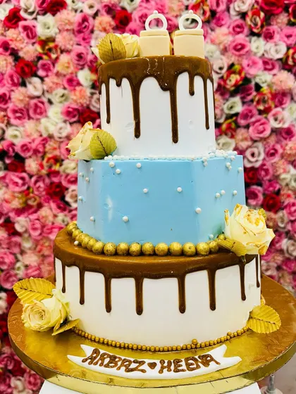 A three-tiered engagement cake in blue and white with a rich caramel drip. The cake is personalized with the couple's name and topped with edible rings.
