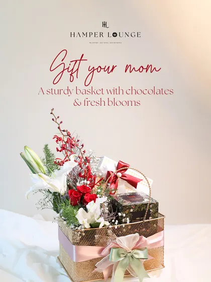 A sturdy and reusable basket filled with luxury treats, gourmet chocolates, and fresh red and white blooms for Mother's Day. It's a warm hug in a box.