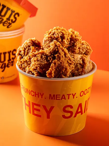 A hero shot of the Louis Burger fried chicken bucket against a bright orange background, making the product look bold and appealing.