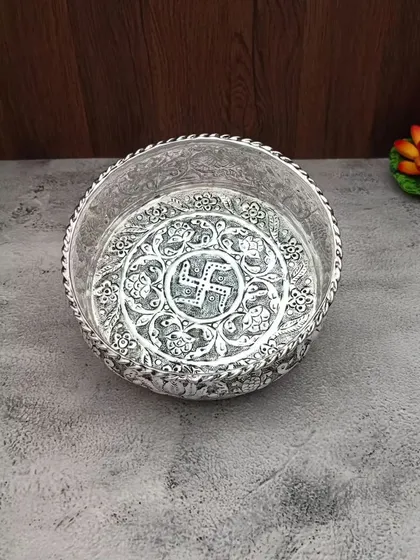 An antique German silver urli with a swastik symbol in the center, surrounded by floral carvings.