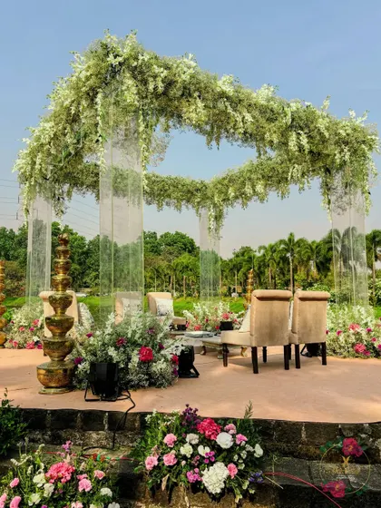 A full view of the modern acrylic mandap set against a serene lake. The transparent pillars give the illusion that the lush floral canopy is floating on air, creating a truly magical setting.