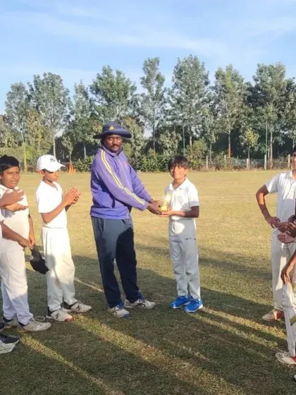 A coach presenting an award to a young player on the field, with his teammates applauding his achievement. We foster a supportive environment for all our athletes.