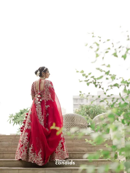 A stunning shot of the bride from behind, looking out over the venue. Her red lehenga stands out, and the composition creates a sense of anticipation and grace.