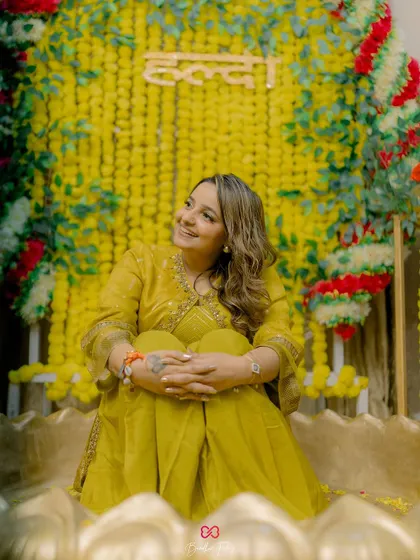 A beautiful portrait of the bride seated against a backdrop of marigolds for her Haldi ceremony, her face glowing with happiness.