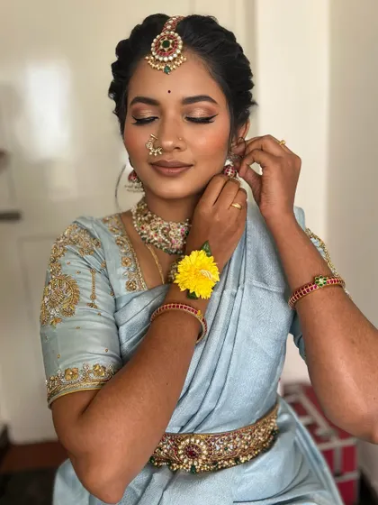 A candid moment as she puts on her earrings. The makeup looks fresh and natural, perfect for a daytime engagement ceremony.