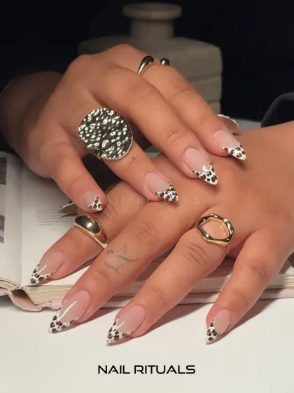 A stylish and trendy nude manicure taken to the next level. This image shows off the glossy finish of our cow print French tips, paired with chunky gold rings.