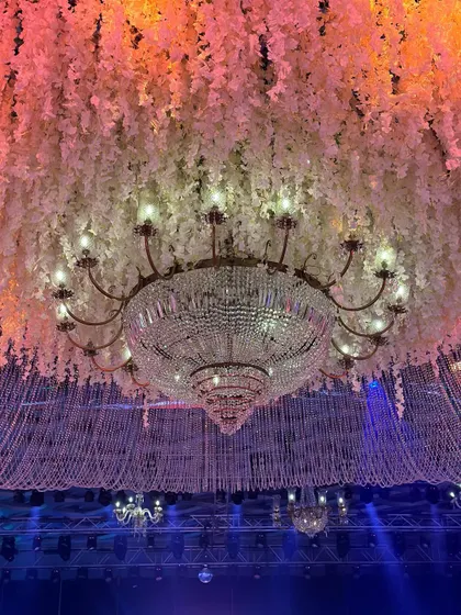 A close-up of a dazzling cascade of crystals and blooms. The combination of a classic crystal chandelier with modern floral and string installations creates a unique and glamorous effect. 💫