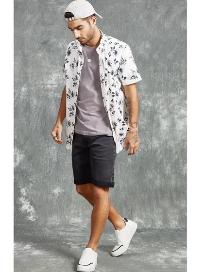 A casual summer look for a men's fashion brand. A floral print shirt is layered over a simple tee with denim shorts, creating an easy, stylish outfit for everyday wear.