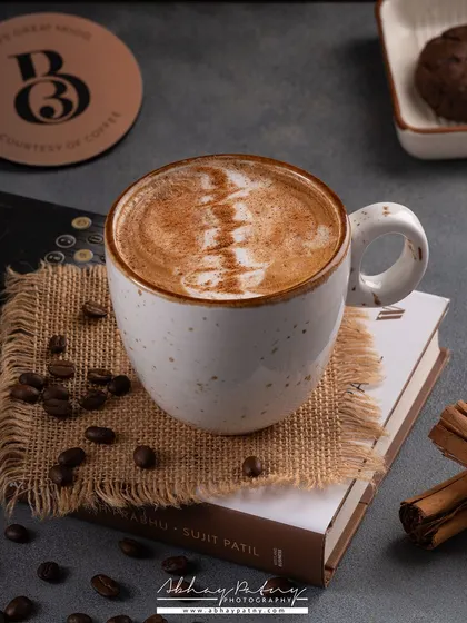 A cozy coffee shot, styled with books and warm tones. The focus is on the rich crema and latte art, appealing to serious coffee lovers.