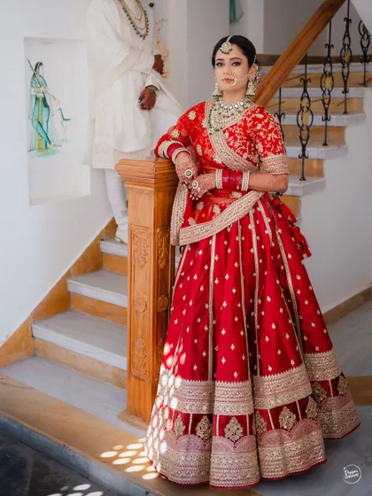 A regal portrait of the bride in her traditional red lehenga, leaning against a staircase in a beautiful Udaipur venue.