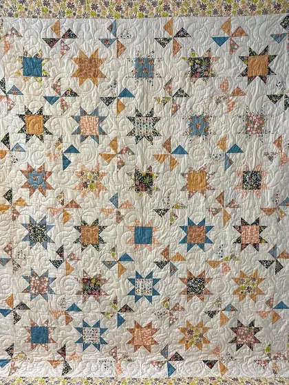 A "Peach Perfection" quilt featuring a mix of star and pinwheel blocks in a soft, peachy color palette.