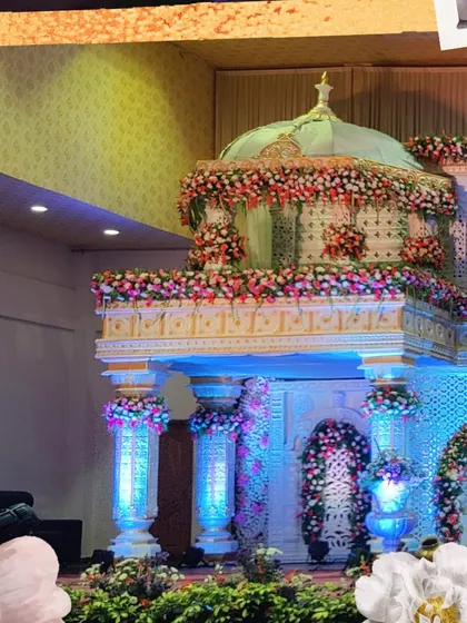 A multi-tiered stage design resembling a floral palace. The structure features a domed top, intricate latticework, and is adorned with an abundance of colorful flowers, creating a truly magical and grand setting.