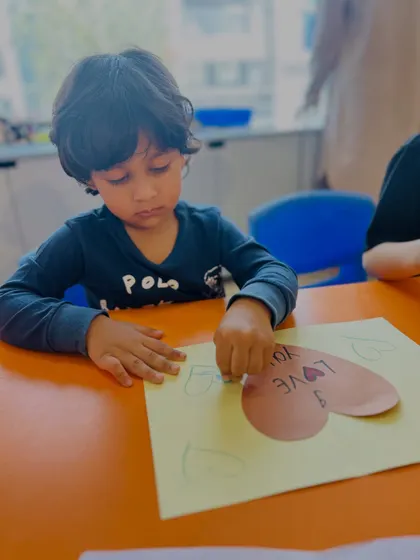 A child carefully colors a heart-shaped card, an activity that combines artistic expression with emotional learning.