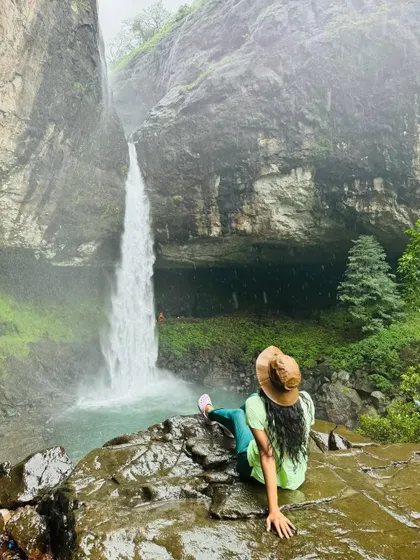 A trekker enjoying the view of the magnificent Devkund waterfall. The green pool and the powerful cascade make for a perfect picture.